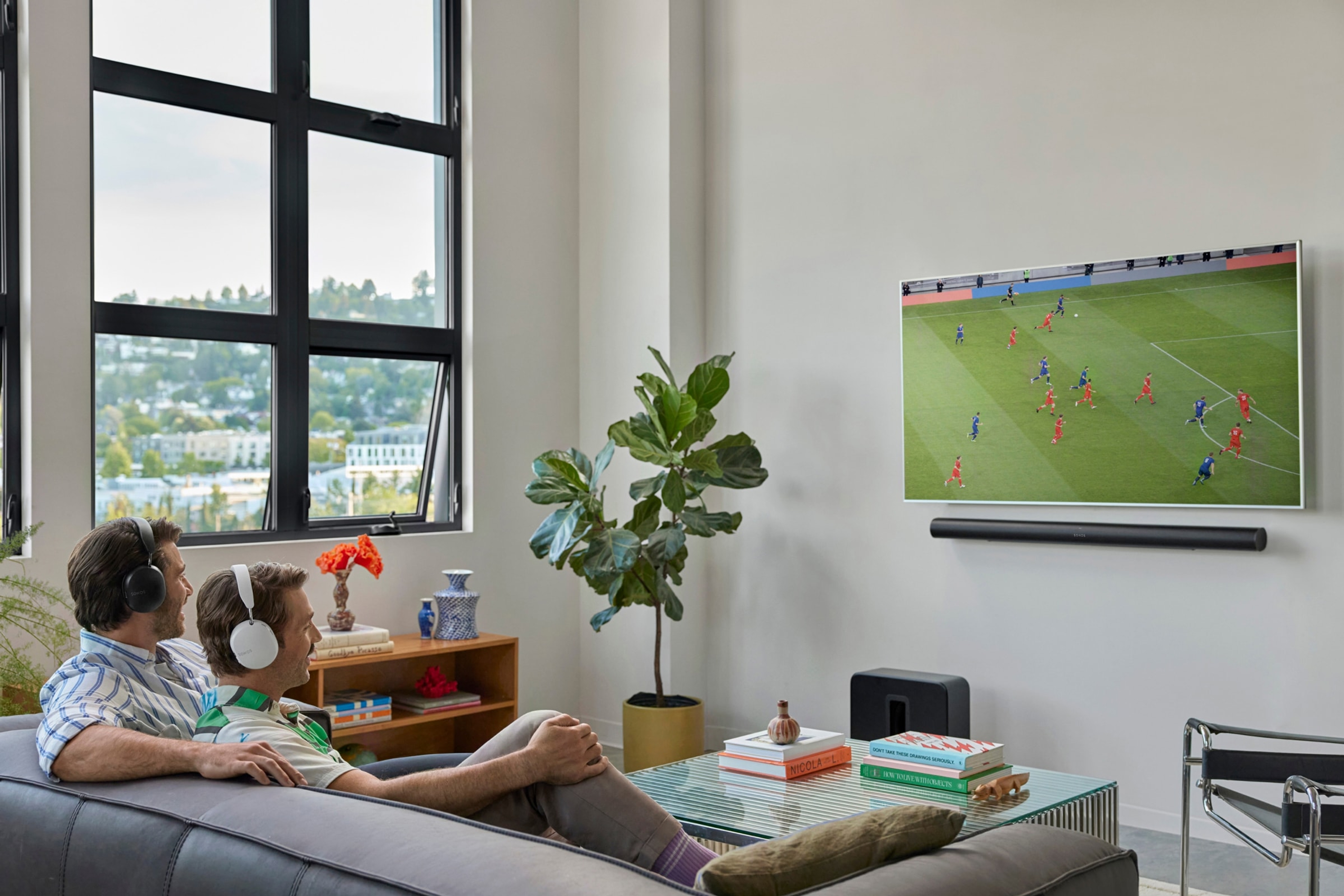 Eine Familie auf einer Couch, die mit einer Arc Ultra in Schwarz und einem Sub 4 in Schwarz fernsieht
